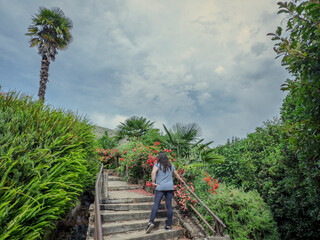 Woman climbing scenic garden stairway under cloudy sky