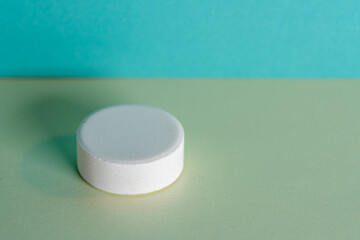Single white medicine tablet laying isolated on green and blue pastel background as macro with...