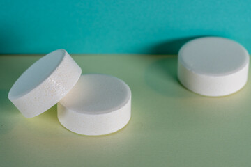 Three white medicine tablets laying isolated on green and blue pastel background as macro 1