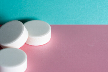 Three white medicine tablets laying unordered isolated on pink and blue pastel background as macro 3