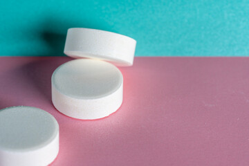 Three white medicine tablets laying unordered isolated on pink and blue pastel background as macro 2