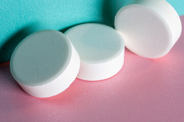 Three white medicine tablets laying unordered isolated on pink and blue pastel background as macro