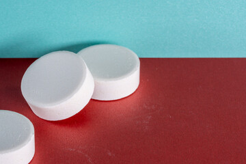 Three white medicine tablets standing isolated on red and blue pastel background as macro with copyspace