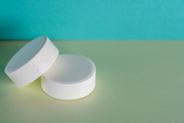 Two white medicine tablets laying isolated on green and blue pastel background as macro with copyspace 1