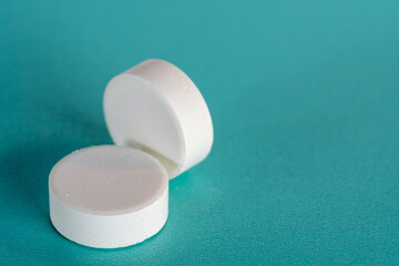 Two White medicine tablets standing and laying on side isolated on blue pastel background as macro