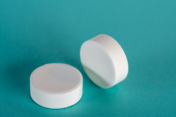 Two White medicine tablets standing and laying on side on blue pastel background as macro 1