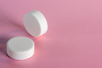 Two white medicine tablets standing on side and laying isolated on pink pastel background as macro 1