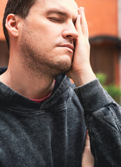 Man Expressing Frustration While Leaning Against His Hand in a Casual Setting During Daylight