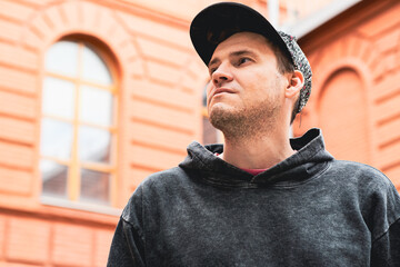 In an urban setting a young man stands confidently against a red brick building He wears a casual...