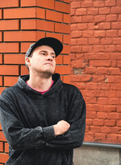 In an urban setting a young man stands confidently against a red brick building He wears a casual...