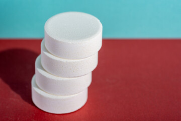 Shifted staple of four white medicine tablets standing isolated on red and blue pastel background as macro with copyspace 1