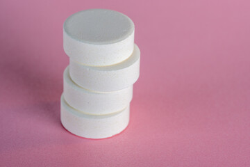 Shifted staple of four white medicine tablets laying isolated on pink pastel background as macro 1