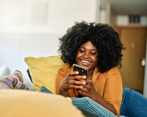 Portrait of a young black woman chatting with girlfriend at home, using modern mobile phone, checking social media, using mobile app, texting or browsing internet on his phone