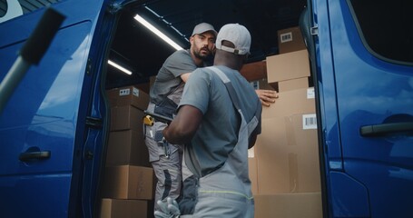 Outside of Logistics Warehouse: Male Employee Unloading Delivery Truck with Cardboard Boxes, Online Orders, Purchases and E-Commerce Goods. African American Manager Using Digital Tablet. Slow Motion.