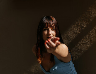 Young caucasian female in blue dress reaching towards camera in dramatic lighting