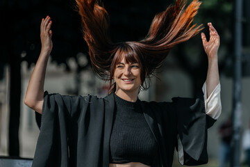 Joyful caucasian young woman with long red hair flipping in the air outdoors