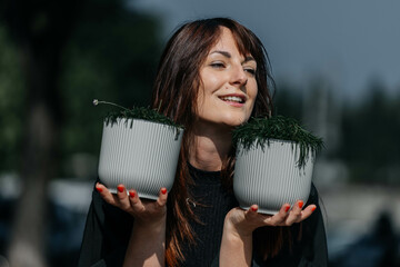 Smiling caucasian young adult female holding potted plants outdoors