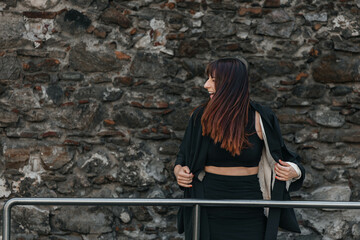 Smiling young female in black outfit by stone wall