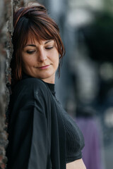 Caucasian female adult with short hair leaning against wall in urban setting