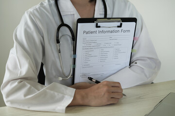 Young asian woman doctor in white uniform with stethoscope taking notes, using laptop, mobile phone, writing in medical journal, professional therapist practitioner filling documents or patient card.
