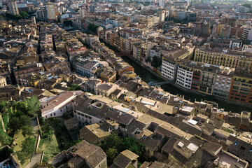 Obraz premium An aerial view of Girona's historic city center, featuring the cathedral, the Onyar River winding through colorful buildings, and ancient city walls amidst lush hills