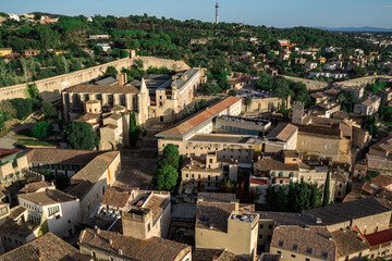 Obraz premium An aerial view of Girona's historic city center, featuring the cathedral, the Onyar River winding through colorful buildings, and ancient city walls amidst lush hills