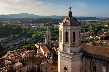 Fototapeta premium An aerial view of Girona's historic city center, featuring the cathedral, the Onyar River winding through colorful buildings, and ancient city walls amidst lush hills