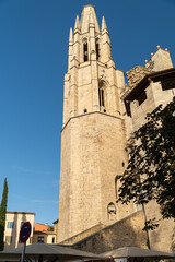 The towering Gothic bell tower of Girona Cathedral stands prominently against a clear blue sky,...
