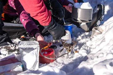 Hikers lighting portable stove to melt snow for drinking water during winter camping trip