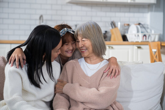 Portrait of three generations of Asian women a cute little girl hugging her mother and grandmother while smiling and enjoying quality family time together at home bonding with love, care, affection - Powered by Adobe