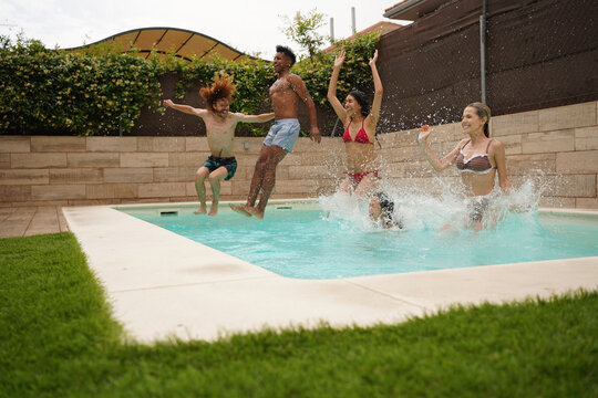 Group of cheerful young friends jumping into a swimming pool, enjoying summer holidays together