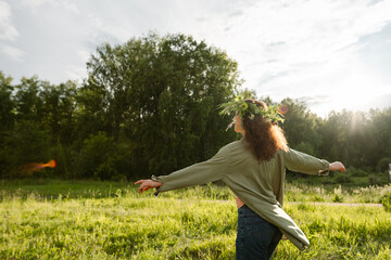 Female with floral crown dancing in countryside field outdoors, back view. Symbol of carefree...
