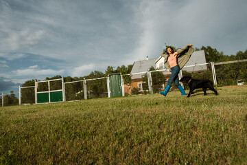 Happy female with pet dog having fun and stepping playfully outdoors in village yard. Represents...