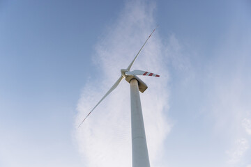 Wind turbine rotating against blue sky with clouds, generating sustainable energy