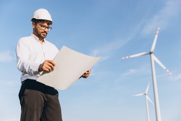 Engineer analyzing blueprints at wind turbine farm for sustainable energy