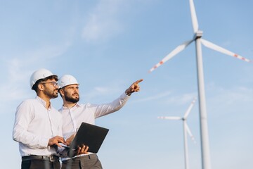 Engineers inspecting wind turbines with laptop in a wind farm
