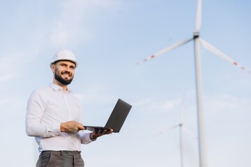 Engineer holding laptop inspecting wind turbines in a wind farm