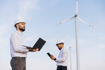 Engineers working with laptop and tablet near wind turbines