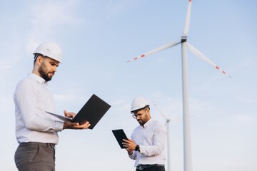 Engineers working with laptop and tablet near wind turbines