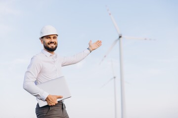 Engineer showing wind turbines in a wind farm with laptop in hand