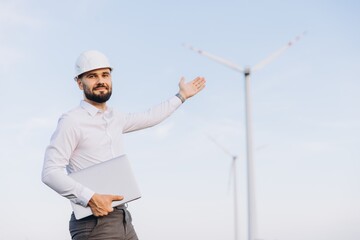 Engineer showing wind turbines in a wind farm with laptop in hand