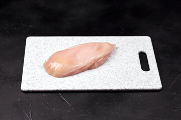 Raw chicken breast fillet placed on a white cutting board, showcasing fresh meat texture and color,...