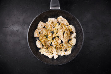 Raw chicken pieces seasoned with spices are arranged in a frying pan on a dark textured surface, showcasing preparation for a delicious meal
