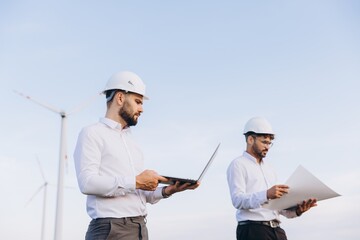 Engineers working on a wind turbine project using laptop and blueprints