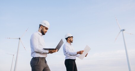 Engineers working in a wind turbine power plant using laptop and blueprints
