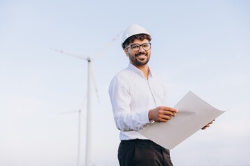Smiling engineer holding blueprint in a wind turbine power plant