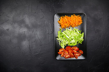 Freshly prepared salad ingredients arranged on a black plate, featuring vibrant orange carrots,...