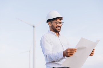 Smiling engineer examining blueprints at wind turbine farm