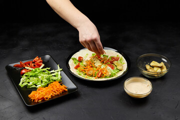 Hand of a person adding fresh ingredients to a colorful salad on a plate, with a variety of...