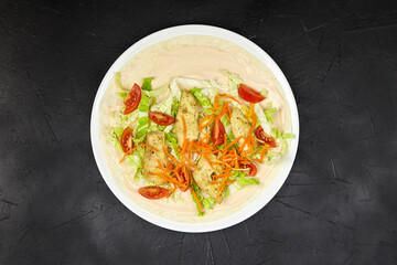 Freshly prepared wrap featuring grilled chicken, crisp lettuce, vibrant tomatoes, and shredded carrots, served on a white plate against a dark textured background, showcasing a delicious meal
